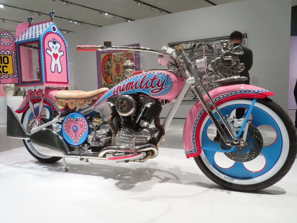 I følge eget utsagn har Grayson Perry bestandig elsket custom sykler og i 2008 hadde han nok penger til å få laget sin egen. Han ønsket å fremstå som et alternativ til den maskuline biker-kulturen så istedenfor macho flammer og nakne kvinner så lakkerte han sykkelen rosa, jentete og leken. På hver side av tanken står ordene Humility (ydmykhet) og Patience (tålmodighet).
 Foto: Jarl Hole